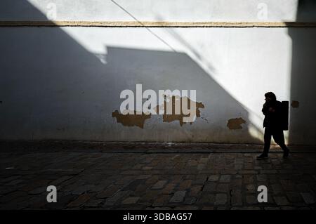 Une personne marche le long des pavés de la rue sol à Séville, Espagne. Les ombres tombent sur le mur alors que le soleil crée un fort contraste sur cette rue. Banque D'Images