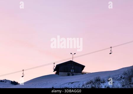 Câbles de téléski sur une pente enneigée au coucher du soleil rose d'hiver Banque D'Images