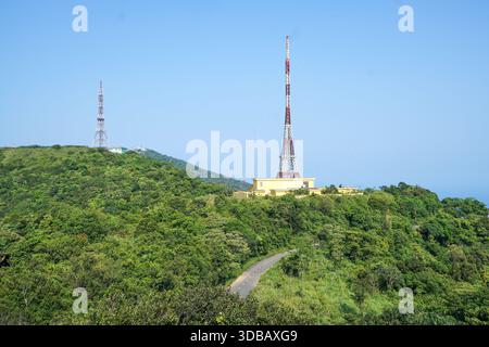 Deux tours de communication se dressent sur une montagne verdoyante sous un ciel bleu clair. Banque D'Images