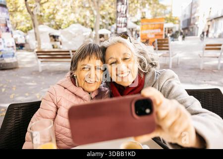 Heureuses femmes âgées amies appréciant le café et prenant un selfie dans un café en plein air Banque D'Images