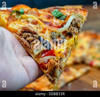 Tranche de pizza au thon avec fromage fondu et légumes tenus à la main, gros plan Banque D'Images
