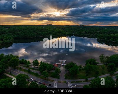 Vue aérienne du scintillant Fresh Pond Reservation reflétant le ciel spectaculaire, avec des arbres luxuriants et le Cambridge Boat Club, Boston, Massachusetts, Banque D'Images