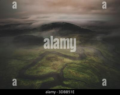 Vue aérienne des voies navigables sinueuses du marais, voilées d'une brume éthérée sous un ciel sombre, un paysage serein mais dramatique se déploie, Gloucester, M Banque D'Images