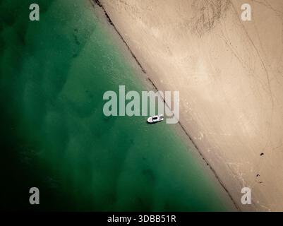 Vue aérienne d'un bateau solitaire reposant sur le bord où l'eau turquoise sombre rencontre la plage de sable brun, Gloucester, Massachusetts, États-Unis. Banque D'Images