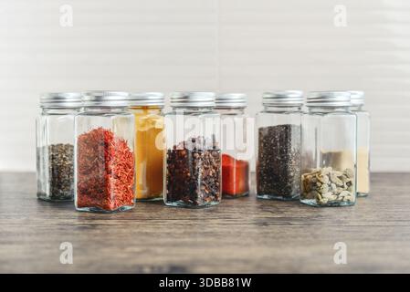 Épices assorties dans des bocaux en verre avec couvercles en métal sur une table de cuisine, vue de face Banque D'Images