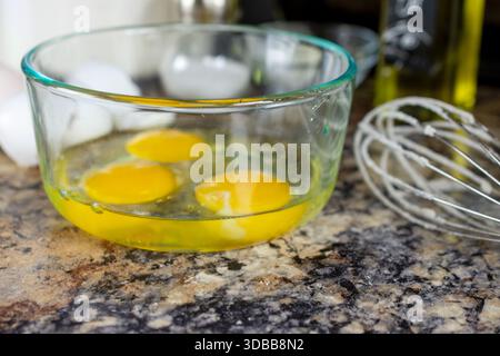 Trois œufs craquelés reposant dans un bol en verre transparent, prêts à être battus et ajoutés au mélange sec de pâte à gaufres pour un petit déjeuner maison à Waukesha Coun Banque D'Images