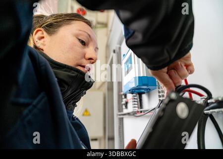Femme ingénieur utilisant la tablette pour vérifier les connexions du panneau électrique avec un collègue Banque D'Images
