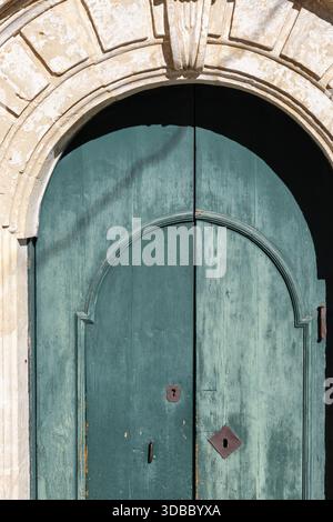 captivant gros plan d'une vieille porte en bois vieillie, peinte sarcelle ou verdigris, située dans une arche en pierre rustique, montrant des lignes symétriques et anci Banque D'Images