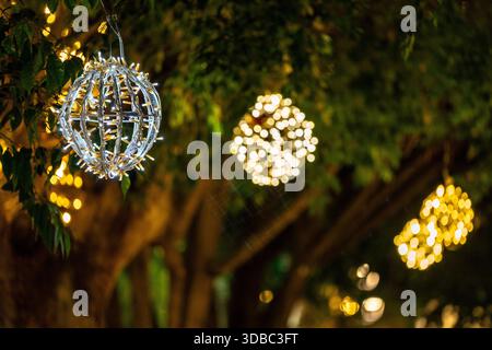 Lanternes sphériques lumineuses suspendues dans les arbres la nuit pendant la saison festive Banque D'Images