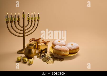 Configuration de célébration Hanukkah. Une menorah, des dreidels, des coffrets cadeaux et des beignets sur fond beige Banque D'Images