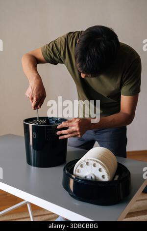 Photo recadrée d'un technicien démontant et effectuant la maintenance sur un humidificateur d'air noir moderne à l'aide d'un tournevis, présentant les composants internes Banque D'Images