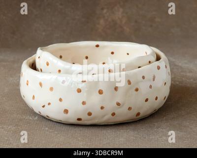 Bols en céramique empilés faits à la main avec glaçage crème brillant et motif à pois bruns sur fond neutre. Produit minimaliste nature morte mettant en évidence un Banque D'Images