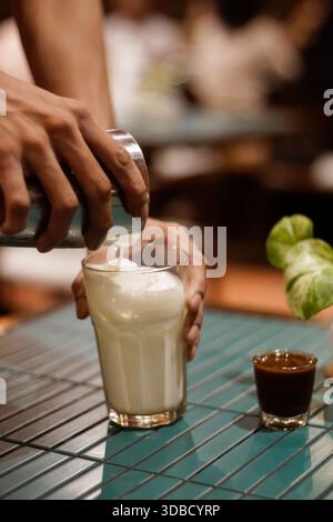 Le barista verse du lait cuit à la vapeur dans un verre pendant la préparation du latte sur le comptoir du café, en gros plan sur le processus de préparation du café Banque D'Images