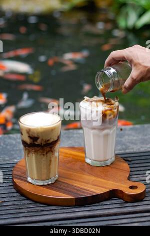 Café glacé et latte glacé servis sur planche de bois, sirop de café versé, ambiance café en plein air Banque D'Images