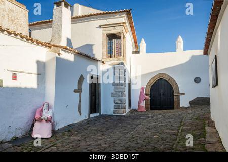 Monsaraz, Portugal - 07 décembre 2024 : vue sur la rue à Monsaraz, Portugal, bordée de vieilles maisons traditionnelles et de deux personnages de la scène de la crèche en plein air. Banque D'Images