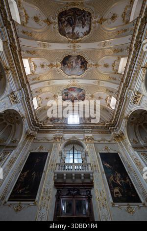 Bergame, Italie - 30 juillet 2025 : vue vers le haut de la nef de la cathédrale de Bergame montrant une voûte baroque richement en stuc, un ornement en or et un grand PAI religieux à l'huile Banque D'Images