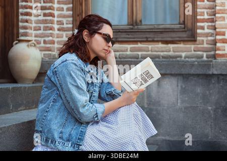 Une jeune femme lit un livre pendant son temps libre dans un vieux bâtiment ; l'image évoque le calme et la joie. Banque D'Images