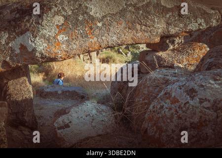 « Gros plan de gros rochers enneigés, avec une personne en arrière-plan explorant le paysage ensoleillé et herbeux. » Banque D'Images