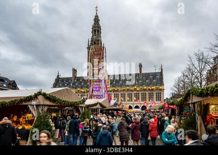 Louvain, Belgique - 14 décembre 2025 : marché de Noël bondé avec stands festifs et grande roue devant la bibliothèque de l'Université KU Louvain pendant Banque D'Images