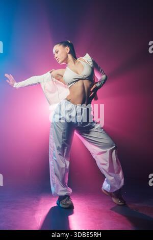 Portrait pleine longueur de jeune femme exécutant un mouvement de danse urbaine avec lumière et brume bleu néon et magenta pour la discothèque et la promotion d'événements Banque D'Images