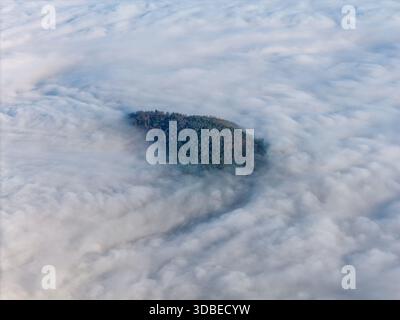 Vue aérienne d'une colline solitaire couverte de forêt s'élève majestueusement d'une mer de nuages blancs moelleux, une île de vert dans un océan sans fin de blanc, O. Banque D'Images