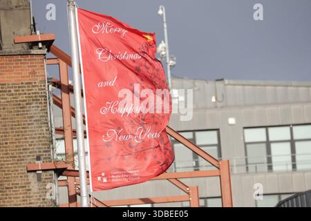 Dublin, Irlande - 10 décembre 2025 - les drapeaux rouge Joyeux Noël et bonne année volent depuis des mâts de drapeau le long des quais de la ville de Dublin, représentant des scènes de rue dans la capitale irlandaise Banque D'Images