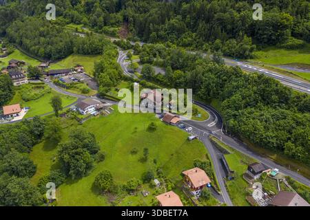 Vue aérienne des prairies verdoyantes rencontrent des forêts denses, coupées en deux par des routes sinueuses menant à des maisons pittoresques aux toits de tuiles rouges, Iseltwald, Canton de Berne, Banque D'Images