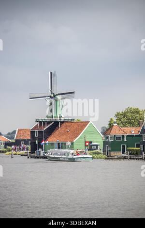 Vue sur une scène hollandaise pittoresque se déroule avec un moulin à vent vert traditionnel dominant des maisons colorées le long d'une voie navigable sereine, Zaanse Schans, Noor Banque D'Images