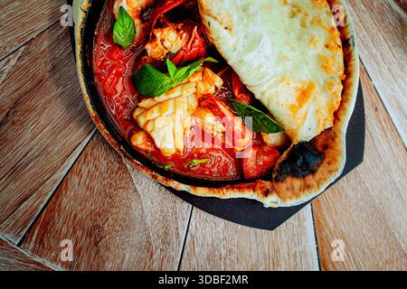 Un ragoût de fruits de mer en croute présente des calmars, des crevettes et du crabe dans une poêle en fonte, accompagnés d'une croûte de pizza avec fromage fondu et poivrons. Le plat i Banque D'Images