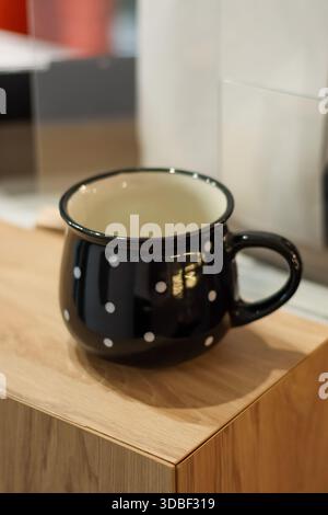 Tasse noire vide en céramique avec taches blanches et rebord beige sur comptoir en bois Banque D'Images