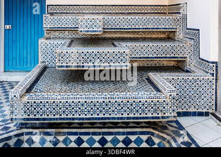 Une impressionnante pièce d'eau intérieure construite à partir de carreaux de mosaïque bleus et blancs. Les marches en couches forment une fontaine géométrique, complétée par une porte bleue vibrante, Banque D'Images