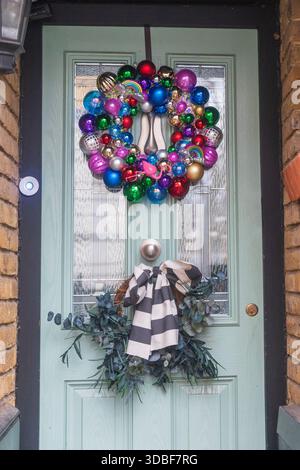 Couronne de noël originale et colorée faite entièrement de boules multicolores et d'une figurine de flamant rose, avec un noeud rayé décoratif ci-dessous, accroché à un Banque D'Images