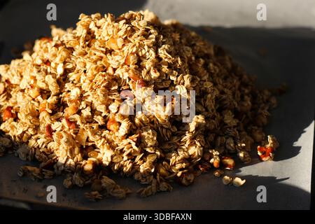 Granola fait maison à base de flocons d'avoine et de noix, empilés sur une plaque de cuisson avec du papier parchemin. Lumière naturelle, tons chauds, concept de petit déjeuner sain Banque D'Images