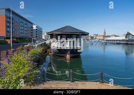 Une frégate licorne historique est amarrée sur un quai à Dundee, contrastant avec le charme maritime ancien et l'architecture urbaine contemporaine. Les eaux calmes reflètent th Banque D'Images