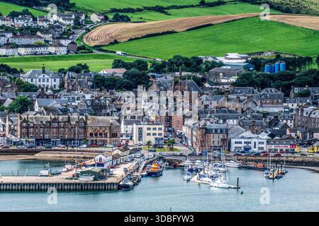 Un pittoresque paysage côtier avec le port de Campbeltown rempli de bateaux, de bâtiments historiques en pierre et de collines verdoyantes en arrière-plan Banque D'Images