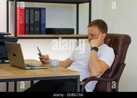 Professionnel contemplatif dans la pensée profonde sur l'appel téléphonique à côté du café dans un cadre de bureau moderne confortable. (96 caractères) Banque D'Images