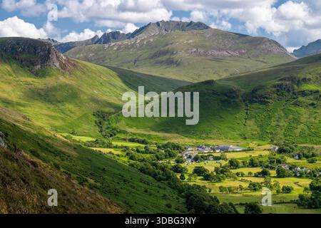 Un paysage écossais panoramique avec des collines verdoyantes, un petit village et des montagnes lointaines sous un ciel lumineux. Parfait pour la nature, voyage, an Banque D'Images
