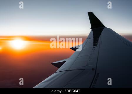Une vue de fenêtre d'avion aérien montre une aile et une ailette dans la lumière du coucher du soleil près de Funchal, Madère, avec un ciel orange et rouge au-dessus des nuages mous pendant un calme Banque D'Images