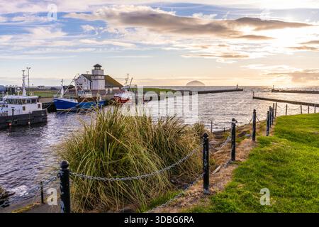 Scène pittoresque du port de Girvan avec des bateaux amarrés le long du quai sous un ciel de coucher de soleil et une côte herbeuse. Banque D'Images