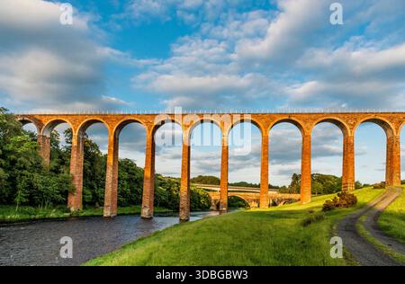 Le viaduc historique de Leaderfoot enjambe une rivière à travers des champs luxuriants sous un ciel bleu. Banque D'Images
