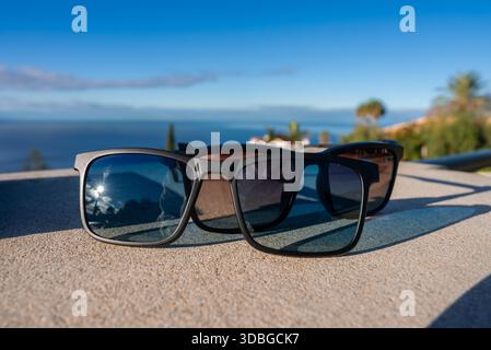 Deux paires de cadres noirs reposent sur un rebord en pierre à Funchal, Madère. L'horizon atlantique, les palmiers et les toits semblent tendres. Une étoile se reflète dans o Banque D'Images