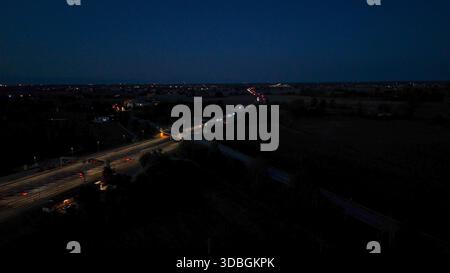 Vue aérienne capturant l'autoroute a21 avec des véhicules circulant la nuit entre Piacenza et Brescia, montrant les traînées légères des voitures et le glo faible Banque D'Images