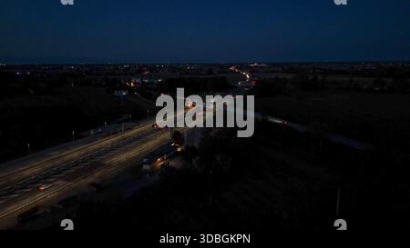 Vue aérienne de nuit de l'autoroute A21 avec des voies éclairées, des voitures et des camions en mouvement à travers un échangeur complexe et une place de péage, montrant transp occupé Banque D'Images