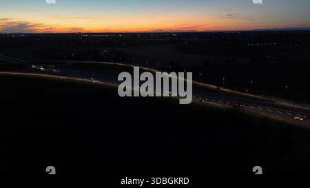 Vue aérienne de nuit montrant le trafic dense sur l'autoroute A21 Piacenza Brescia pendant le coucher du soleil, voitures et camions se déplaçant le long éclairant la route avec th Banque D'Images
