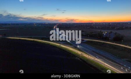 Vue aérienne de suivi des voitures et des camions circulant sur l'autoroute A21, une voie de transport importante, avec un pont supérieur éclairé par la rue Li Banque D'Images