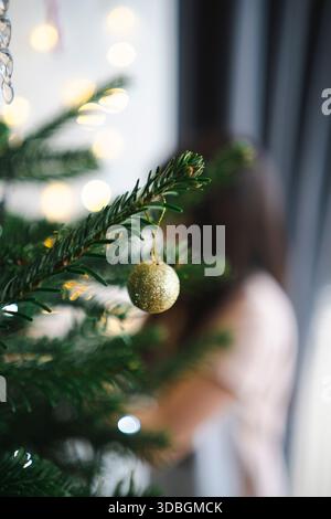 Image floue de fille décorant l'arbre de Noël en mettant l'accent sur la branche et l'ornement, concept de vacances festives Banque D'Images