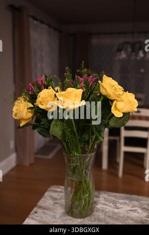 Un bouquet floral vibrant avec des roses jaunes douces et des fleurs magenta vives disposées dans un vase en verre clair sur un fond sombre. Banque D'Images
