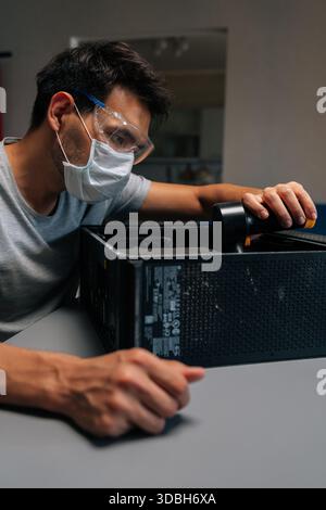 Portrait vertical de technicien informatique dans le masque de protection et l'unité de système de nettoyage de lunettes de sécurité avec vide pendant la maintenance matérielle de précision. Banque D'Images
