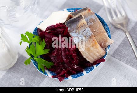 Salade de hareng appétissante avec betteraves, crème sure et persil dans une assiette blanche Banque D'Images