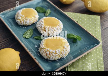 Biscuits craquelés au citron avec du caillé de citron sur plaque rectangulaire bleue sur fond en bois avec des citrons frais, gros plan Banque D'Images